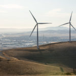 two wind turbines on a hill overlooking a town